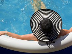 Devojka sa šeširom za sunce leži u gumenom bazenu i pije piće