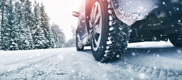 Vozač vozi automobil kroz teško prohodne puteve na planini dok pada sneg. Iza sebe ostavlja trag zimskih guma