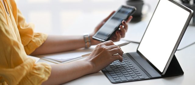 dodaci-za-tablet-futrola-sa tastaturom Ženska ruka u jednoj ruci drži pametni telefon, a drugom kuca na tastaturi tableta koja je deo futrole
