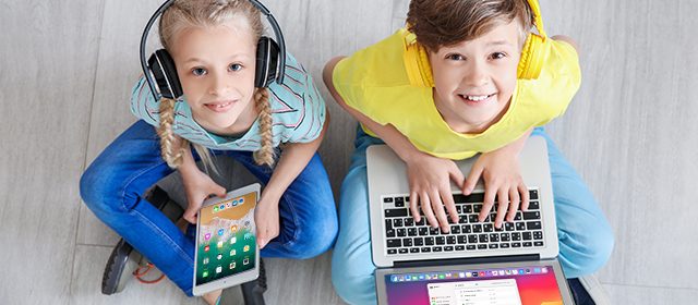 decak-i-devojcica Dečak i devojčica sede na podu i nasmejani koriste slušalice, tablet i laptop
