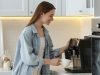 Devojka priprema kod kuće kafu koristeći aparat za kafu u kuhinji