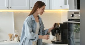 Devojka priprema kod kuće kafu koristeći aparat za kafu u kuhinji