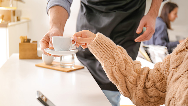 Konobar u kafiću poslužuje devojku u džemperu kafom