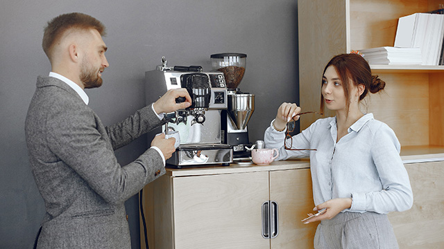 Dvoje zaposlenih razgovaraju u firmi ispirajući kafu na pauzi pripremljenu pomoću aprata za espresso