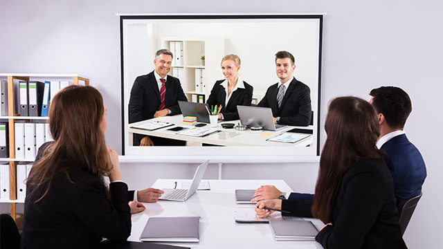 Zaposleni sede u kancelariji i prisustvuju online sastanku koristeći projektor